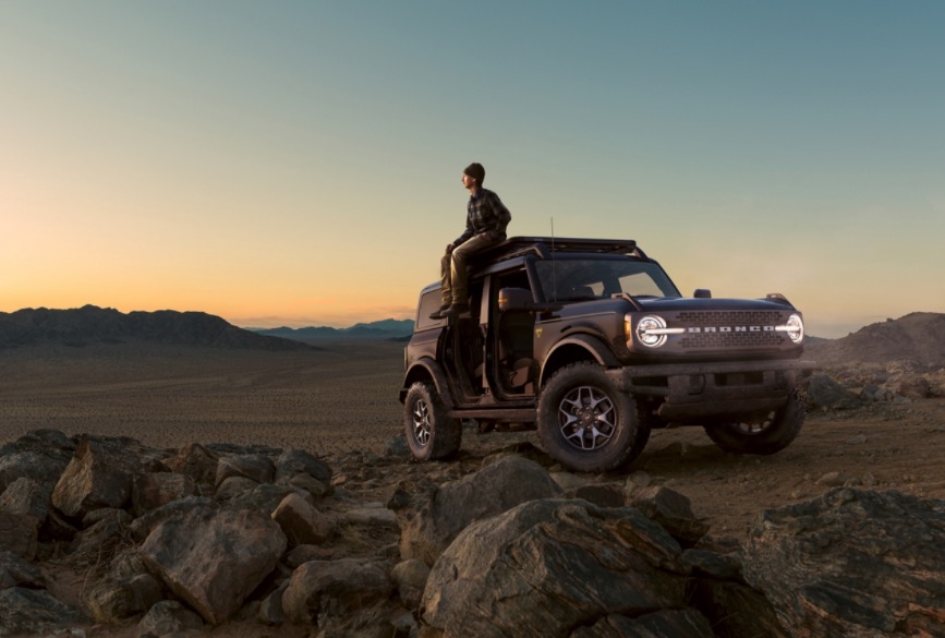 guy sitting on the roof of his Ford Bronco looking at a sunset